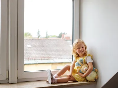 Child sitting in window holding stuffed toy