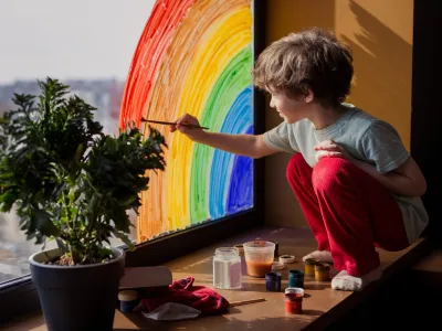 Child painting rainbow on window